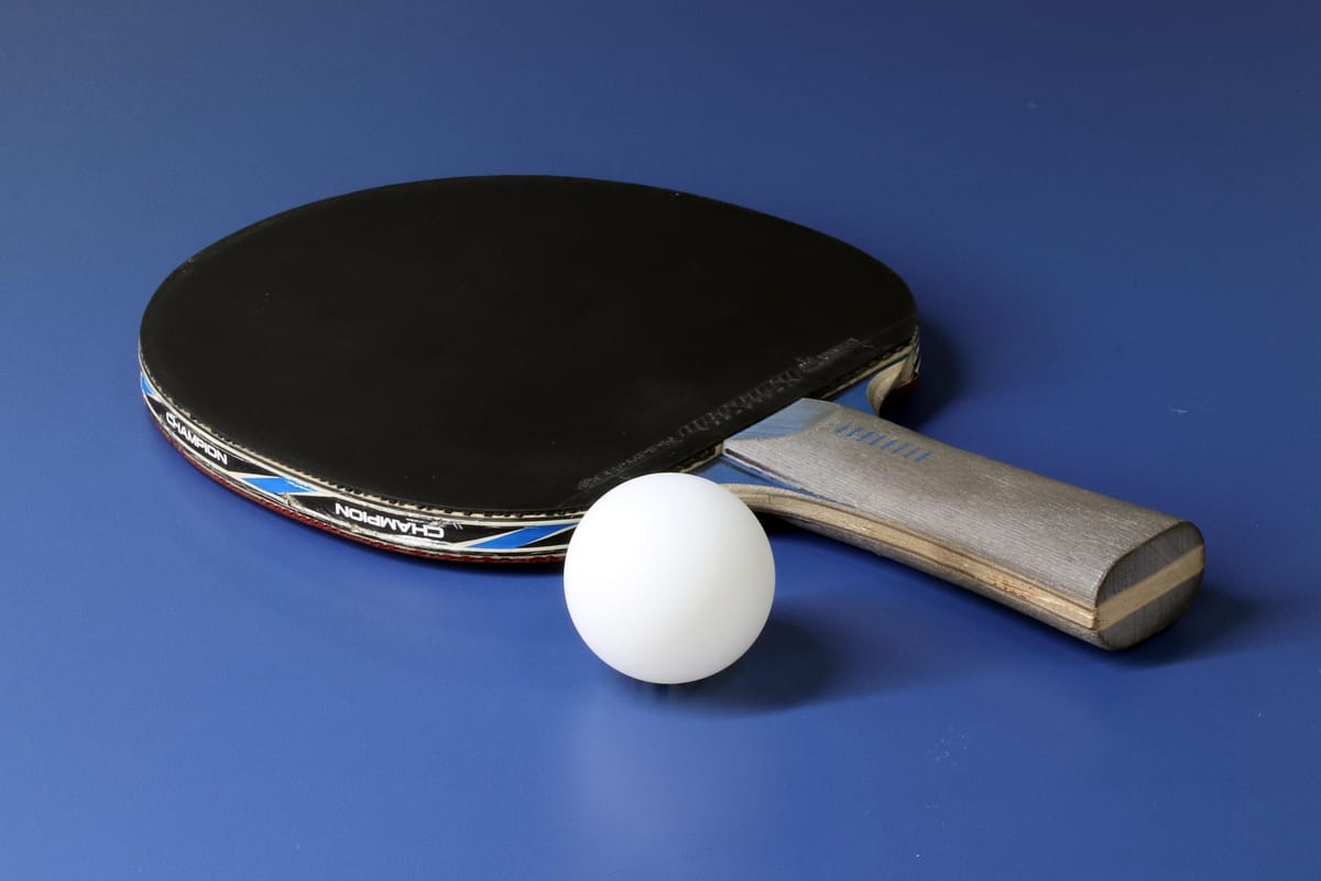 Raquette de tennis de table posée sur une table bleue, la tranche laisse voir le bois et l'épaisseur du revêtement