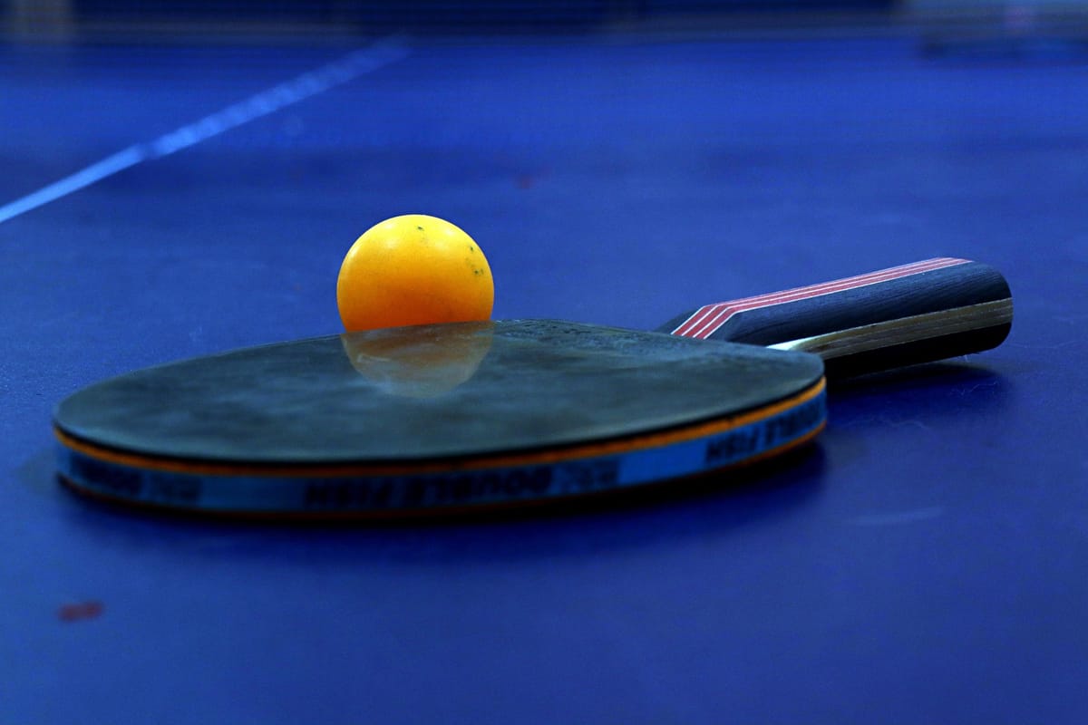 Raquette de tennis de table au revêtement usé et balle orange posées sur une table